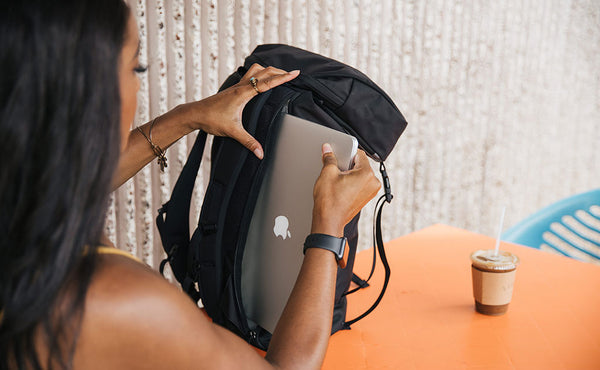 Woman pulling her 15" Apple laptop out of the exterior side-access laptop compartment of her Shadow Guide 33 backpack.